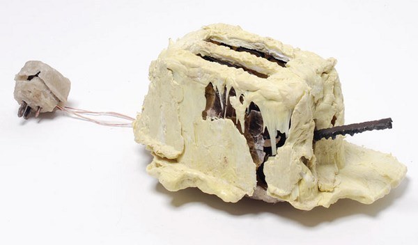 Thomas Thwaites' homemade toaster: a lumpy appliance with a rough, cracked beige potato-starch shell, exposed metal parts, and a bare wire running to a crude plug.
